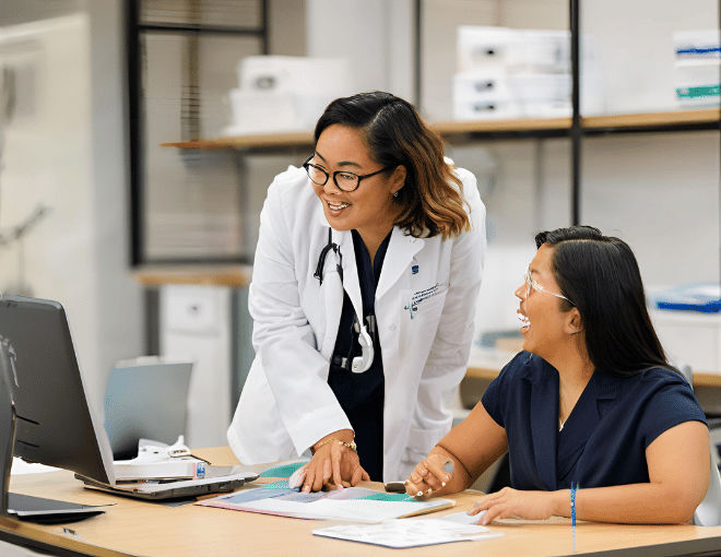 A science professor in a white lab coat speaks to a digital marketing expert in preppy office attire seated at a laptop, discussing collaborative strategies to promote science education.